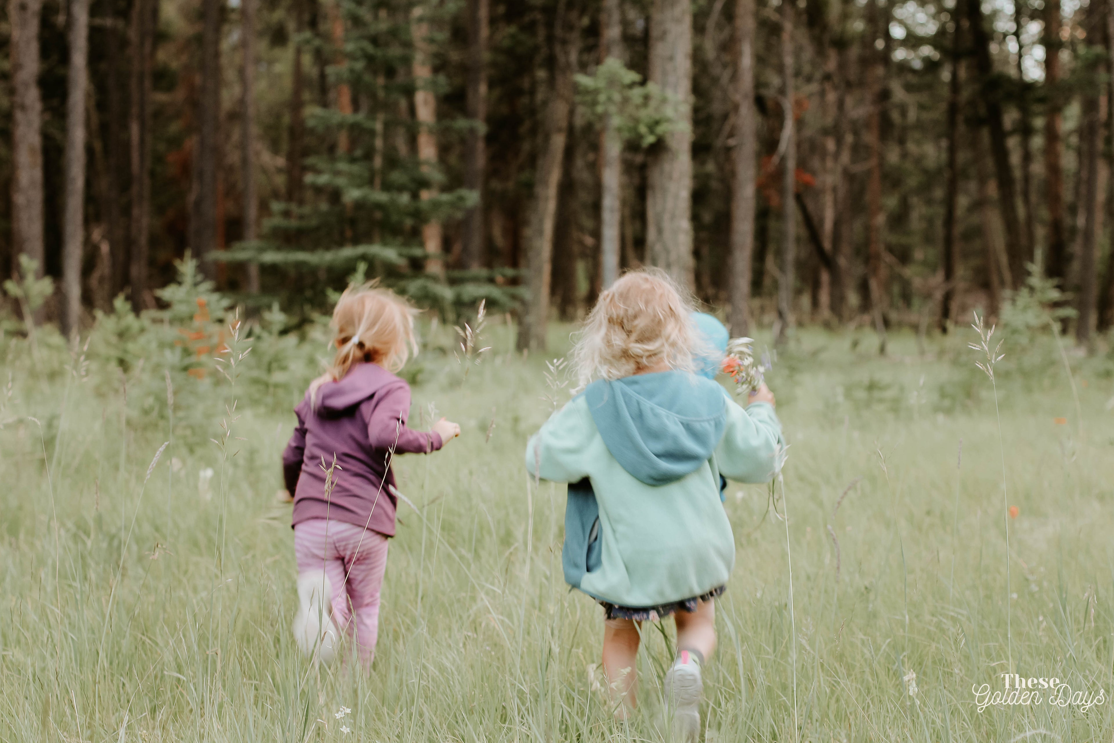 Two children running through a grassy field with trees in the background