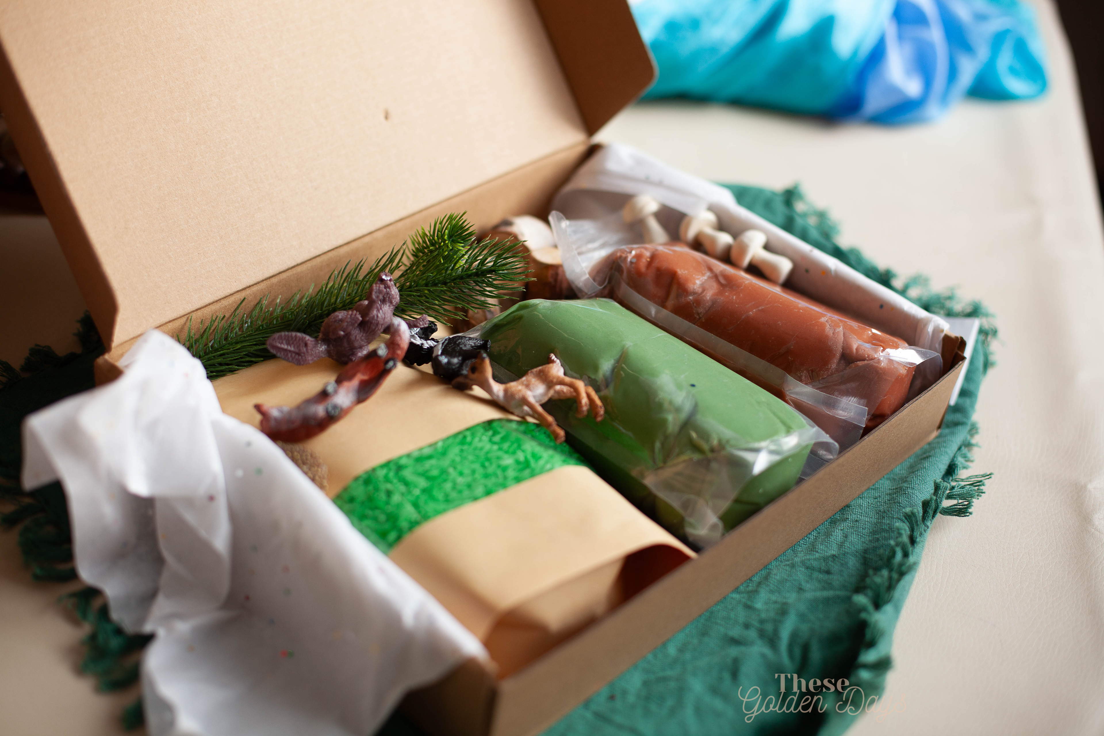 Forest figurines, playdough and rice in a box on a green cloth.