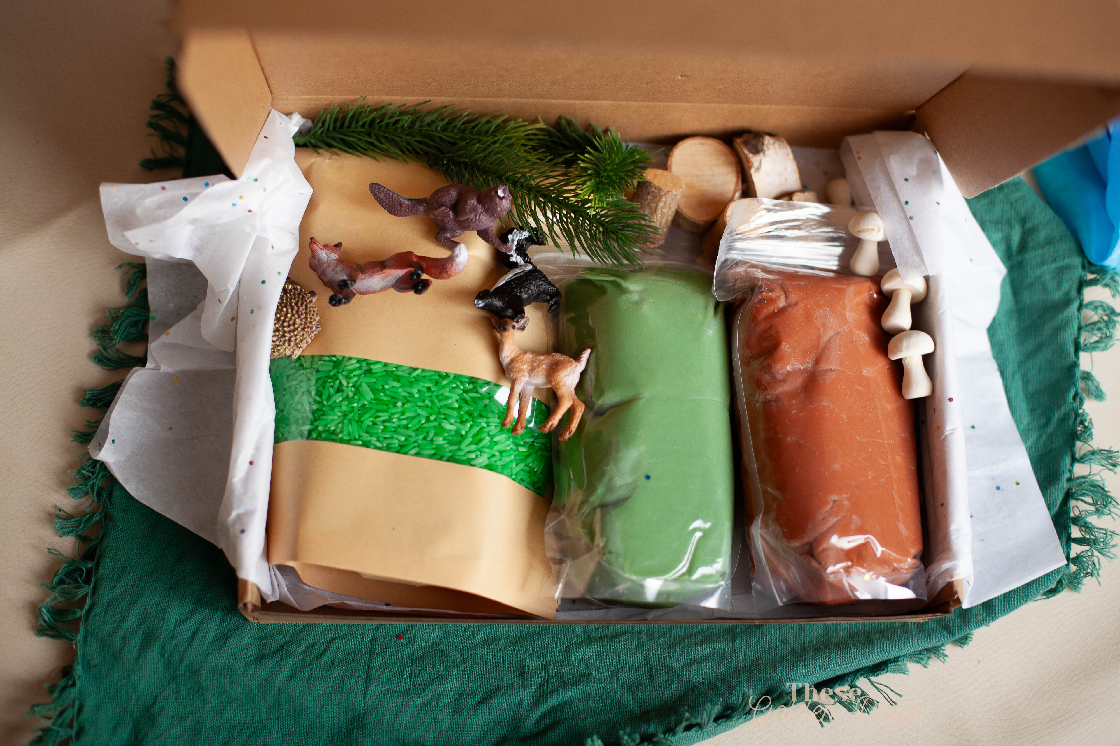 Toy figures, playdough and rice packets in a box on a green fabric background