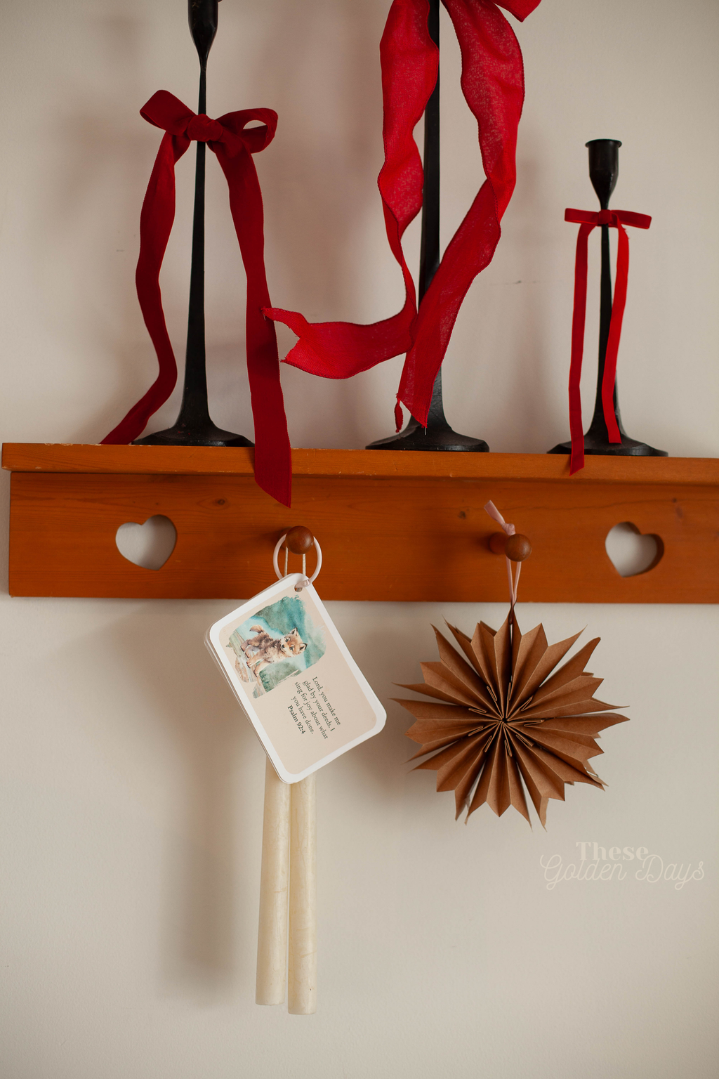 Decorative setup with red ribbons, black candlesticks, and a wooden shelf on a light-colored wall.